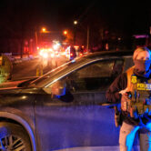 Federal immigration officers stand beside a vehicle at night as emergency lights illuminate a residential street in Minneapolis.