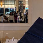 A high school graduate wearing a graduation cap stands with a companion at a restaurant celebration.