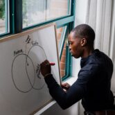 A man makes a Venn diagram on a whiteboard leaning against a windowsill.