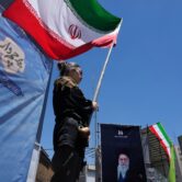 A woman holds an Iranian flag during a pro-government gathering in Tehran, with a large portrait of the late Ayatollah Ali Khamenei displayed nearby.